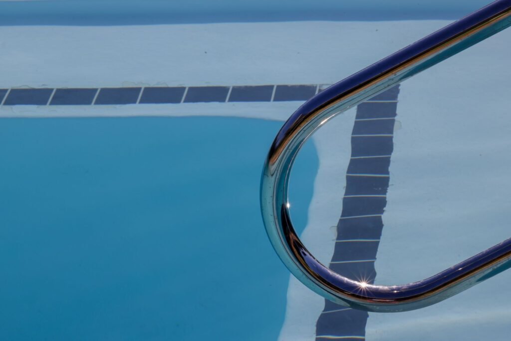 Vista dinámica de una piscina con escalera que refleja la luz del sol sobre la superficie del agua.