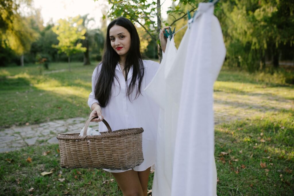 Una mujer al aire libre en un día soleado, llevando una cesta de ropa sucia con sábanas blancas.