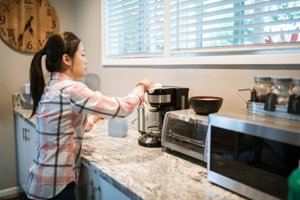Mujer limpiando una cafetera en una cocina moderna y brillante con electrodomésticos.