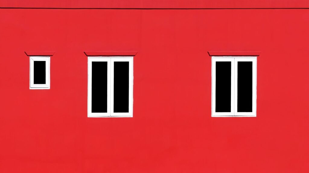 Primer plano de una pared roja vibrante con ventanas blancas minimalistas.