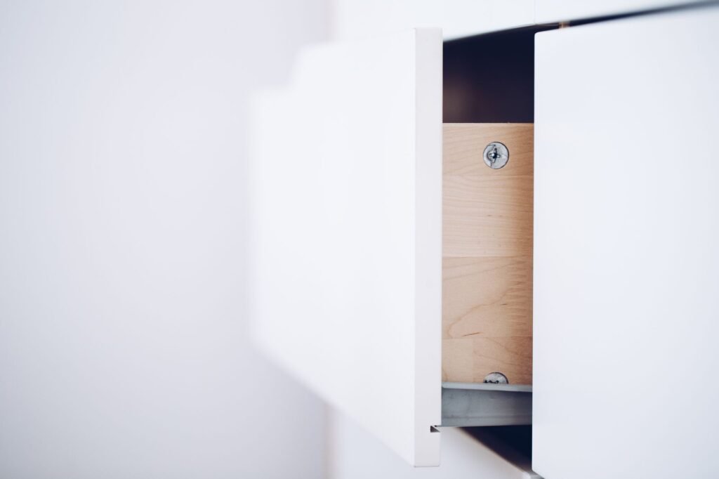 Acercamiento de un cajón blanco abierto que revela un interior de madera y tornillos en un diseño minimalista.