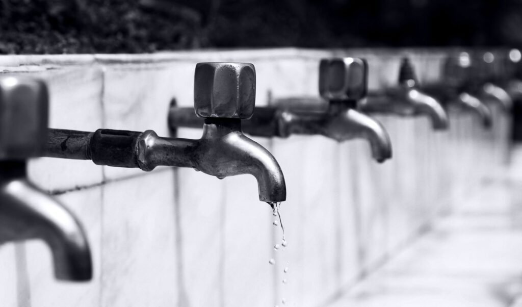 Imagen en blanco y negro de una fila de grifos con agua goteando, resaltando detalles de fontanería.
