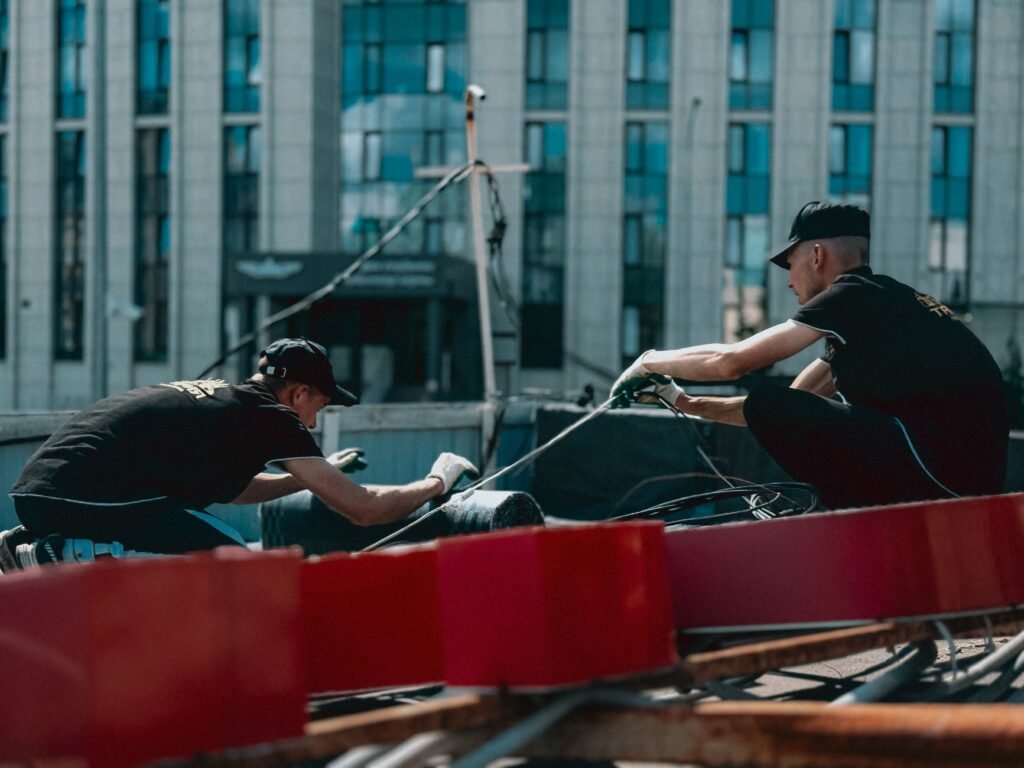 Dos trabajadores están realizando trabajos de mantenimiento en una azotea con el fondo de un edificio urbano.