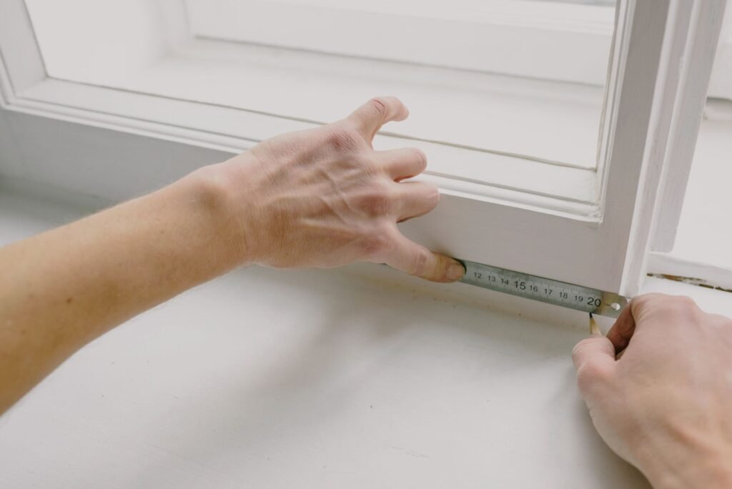 Acercamiento de manos usando una cinta métrica en el borde de una ventana, ideal para temas de renovación y mejoras del hogar.