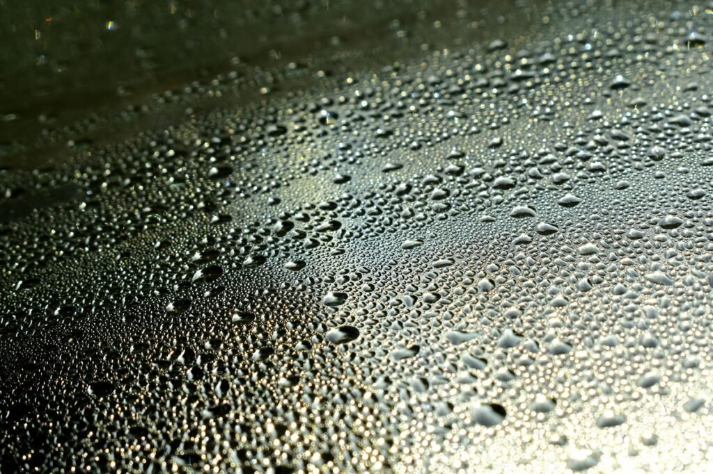 Toma macro de gotas de rocío formando patrones intrincados en una superficie, resaltando textura y liquidez.