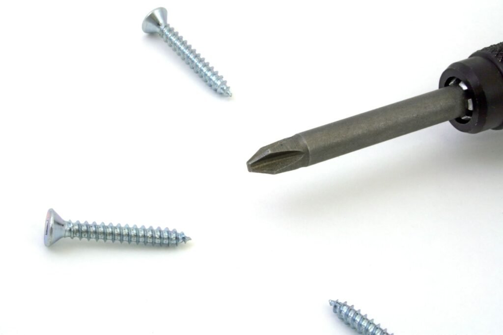 Una vista detallada de un destornillador con tornillos esparcidos sobre una superficie blanca, ideal para temas de herramientas o mantenimiento.
