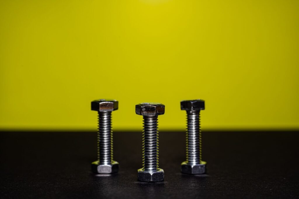 Imagen en primer plano de tres pernos de acero en posición vertical contra un fondo amarillo contrastante.