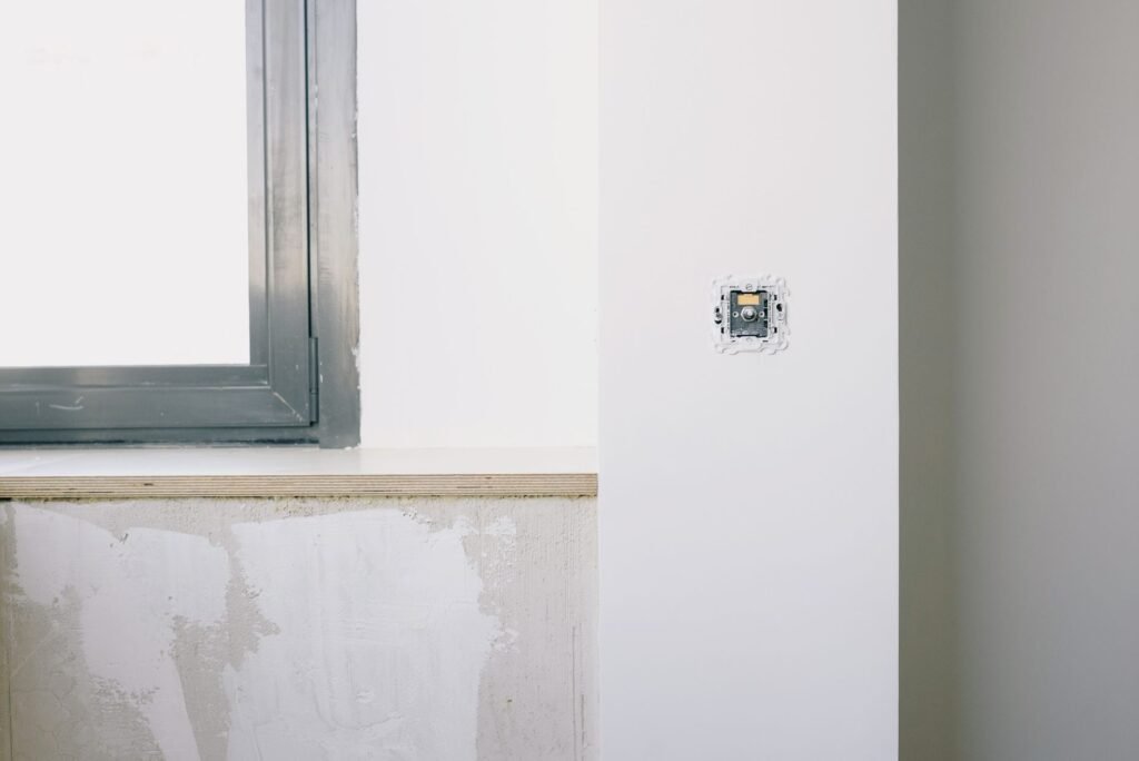 Una habitación minimalista moderna en renovación que muestra la instalación de un interruptor de luz y una gran ventana.