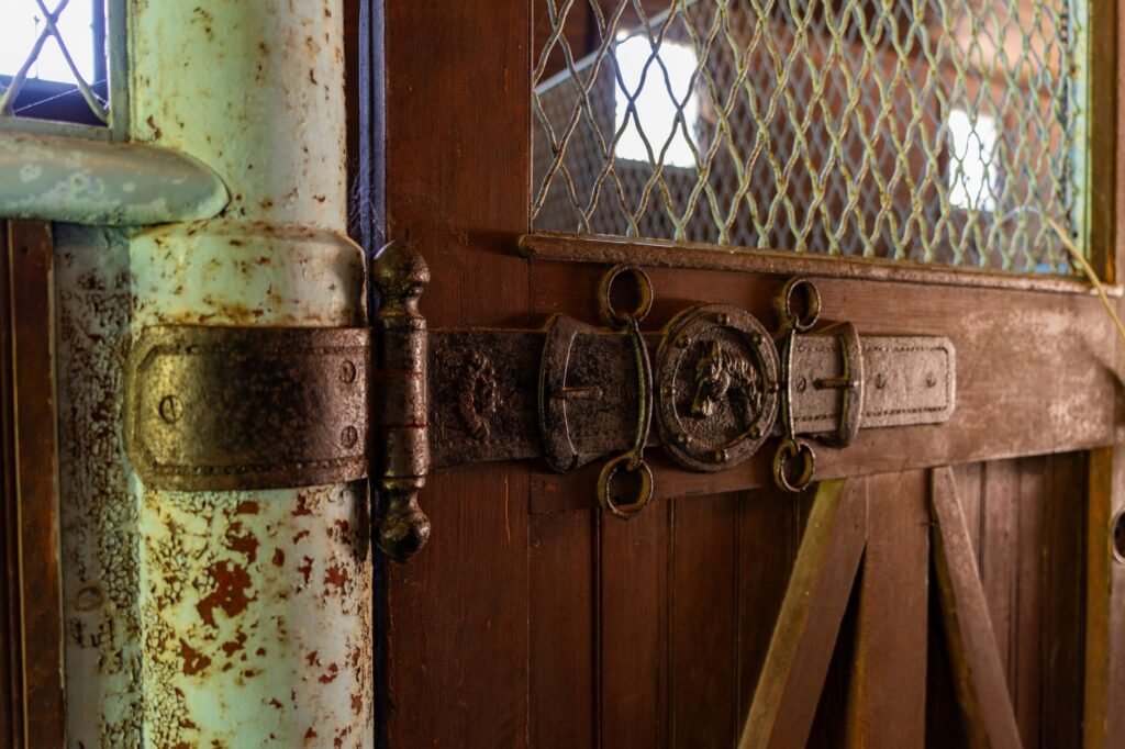 Primer plano de una puerta de granero envejecida con una bisagra de hierro vintage con detalles decorativos.