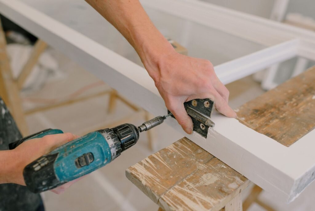 Un manitas usando un taladro para instalar una bisagra en un marco de madera en interiores.