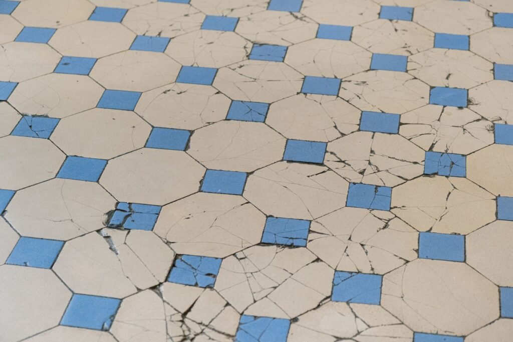 Una vista detallada de baldosas antiguas y agrietadas con un patrón geométrico en azul y blanco.
