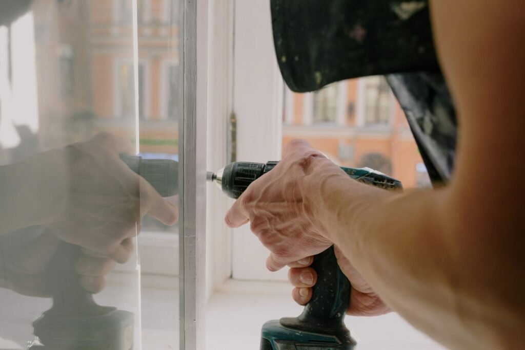 Primer plano de las manos de un profesional usando un taladro para reparar una ventana dentro de un apartamento.
