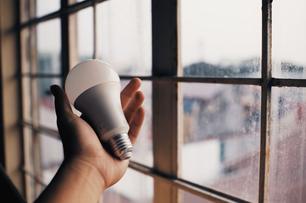 Anonymous person holding energy efficient light bulb in hand on blurred background of big dusty window in light room