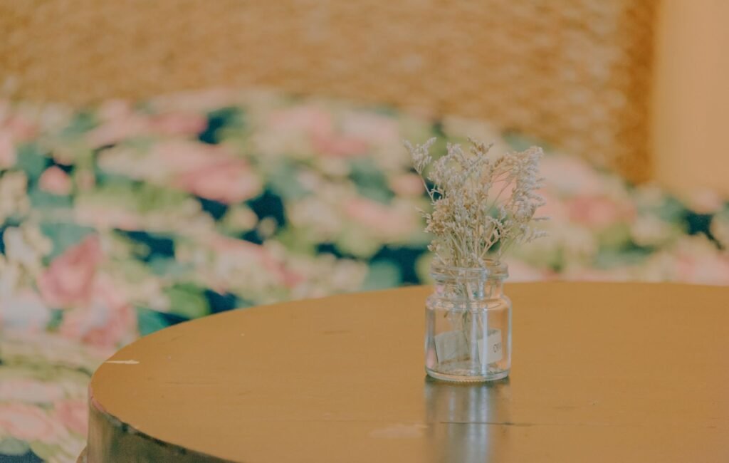 Aesthetic arrangement of dried flowers in a glass jar on a round wooden table.