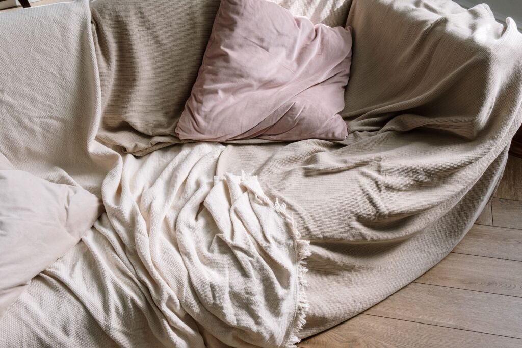 Inviting beige sofa with plush pillows and a warm blanket draped over wooden flooring.