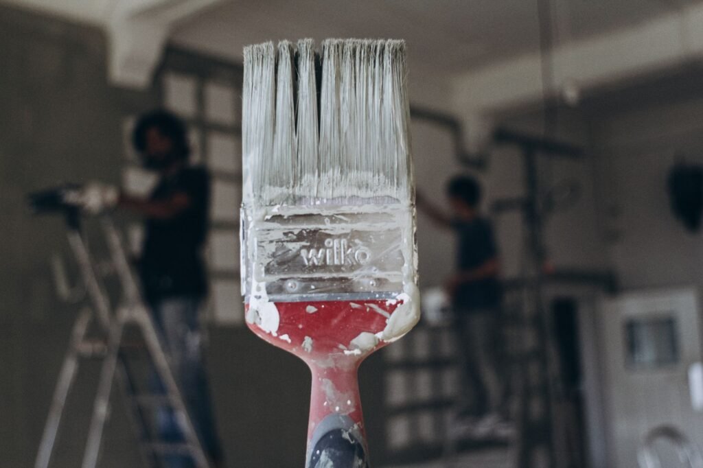 Detailed close-up of a paintbrush with men painting a wall in the blurred background, highlighting renovation work.